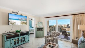 A living room with a TV, a green cabinet, a patterned sofa, and a balcony with a view. - Beach Walks, Sunset Views & Coastal Bliss – Islander 417 (Destin)