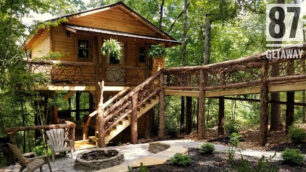 Un chalet rustique avec un escalier en bois menant à une terrasse, entouré d’arbres et agrémenté d’un foyer en pierre.
