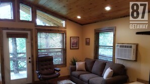 Une pièce chaleureuse avec un plafond en bois, un fauteuil en cuir marron, un canapé marron, une petite commode en bois et une baignoire blanche.