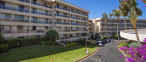 A multi-story hotel with balconies, a parking area, and a well-maintained lawn.
