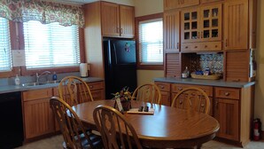 A kitchen with wooden cabinets, a black refrigerator, a dining table with chairs, and a window with blinds. - Rural Retreat yet close to the sites. Cedar point*Jet Express* African Safari (Port Clinton)