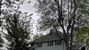 A two-story house with a front porch, surrounded by a well-maintained lawn and large trees. - Rural Retreat yet close to the sites. Cedar point*Jet Express* African Safari (Port Clinton)