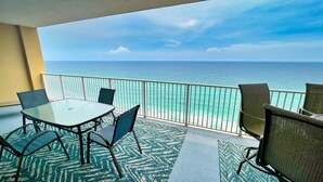 Un balcón con una mesa y sillas de vidrio, con vista al mar turquesa y cielo despejado.