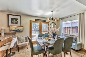 A dining area with a table set for four, chairs, a chandelier, and a view through the glass doors.