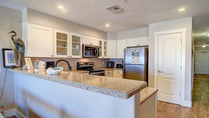 A modern kitchen with granite countertops, white cabinets, stainless steel appliances, and a built-in island. - Poolside, spacious and bright! Community boardwalk access to beach (Port Aransas)