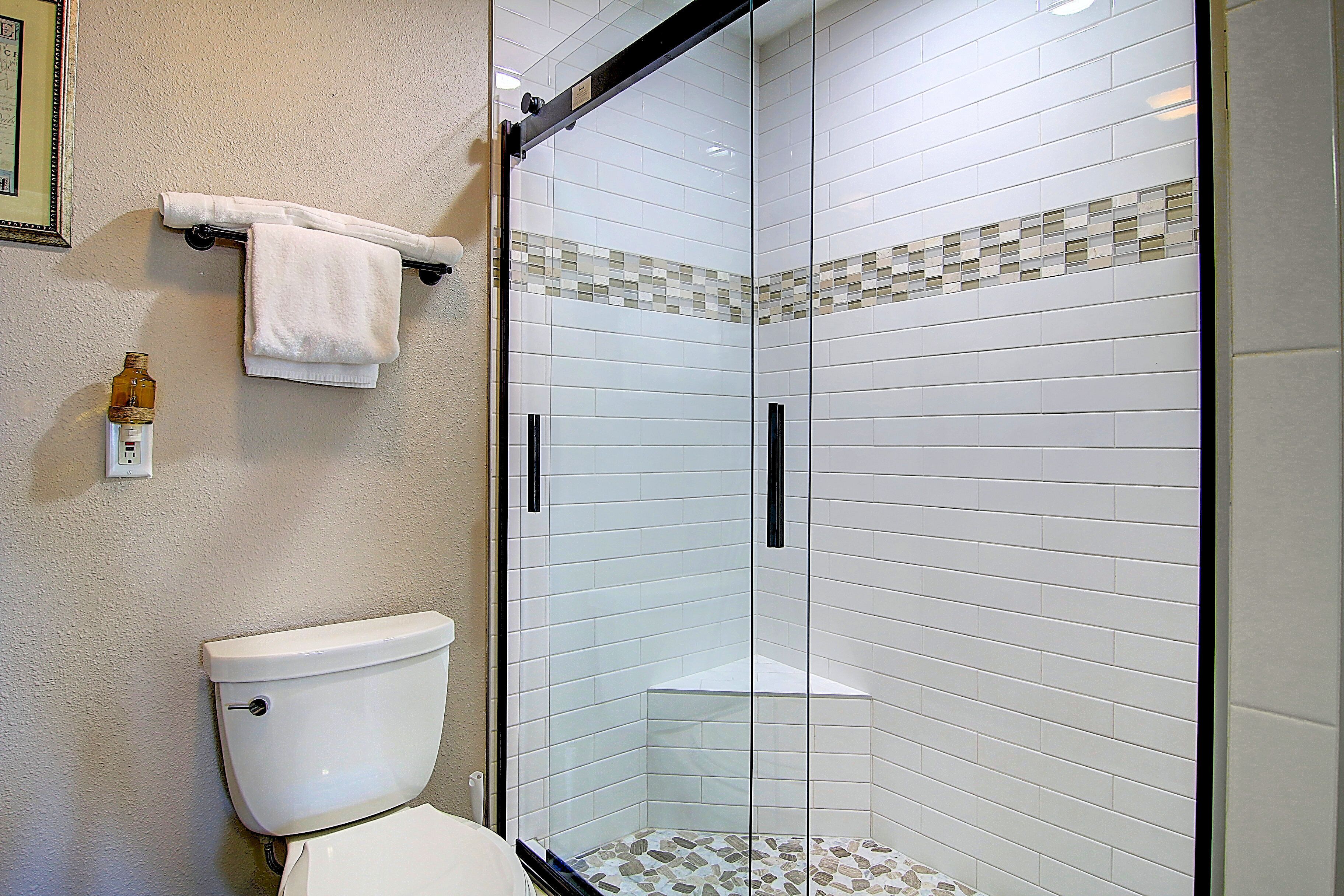 A bathroom with a glass-enclosed shower, white tiles, and a toilet.