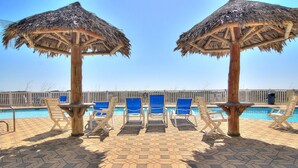 A poolside area with thatched umbrellas, blue lounge chairs, and a tiled floor. - Poolside, spacious and bright! Community boardwalk access to beach (Port Aransas)