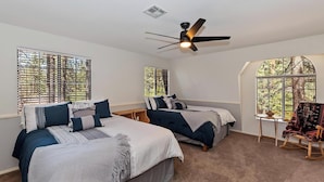 Une chambre avec deux lits, un ventilateur de plafond et de grandes fenêtres équipées de stores.