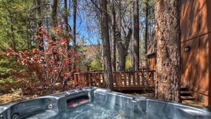 Un bain à remous situé dans une zone boisée, avec une terrasse en bois et un chalet en arrière-plan.