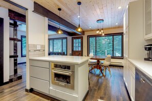 Cocina moderna con una isla grande, hornos integrados, iluminación colgante y ventanas amplias que ofrecen vistas al exterior.