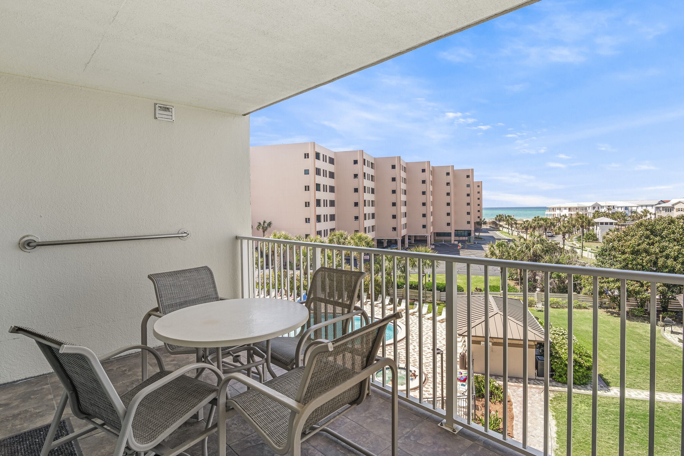 A balcony with a table and chairs, overlooking a pool and buildings.