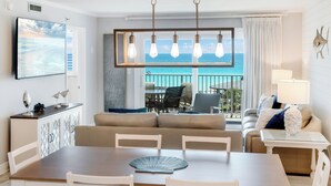 A modern living room with a dining area, a view of the ocean, and a balcony with outdoor seating. - 🌊Islander #509 – Where the Sand is the Softest & the Views Are Endless🏖️✨ (Destin)
