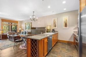 A kitchen with a central island, wooden cabinets, a stainless steel refrigerator, and a dining area with a chandelier.