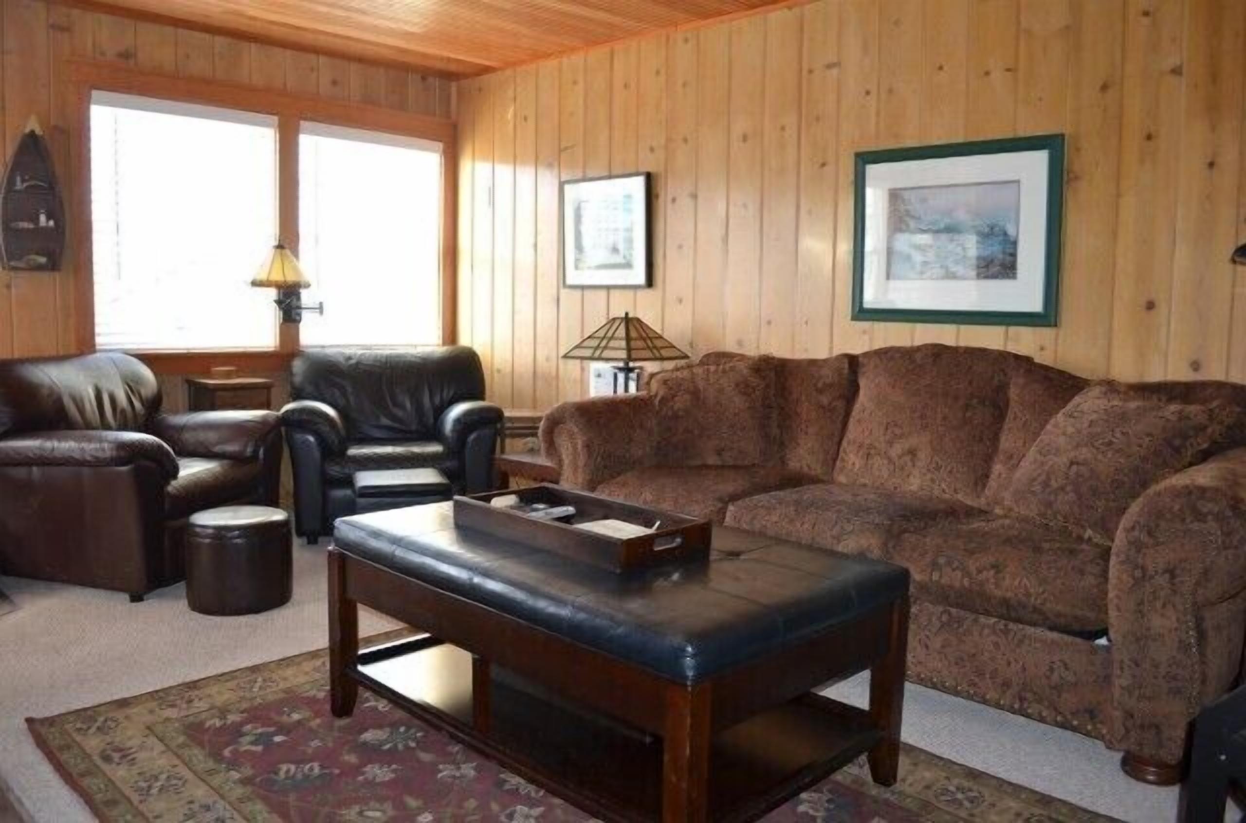 Een gezellige woonkamer met een bruine sofa met patroon, een leren fauteuil en een houten salontafel.