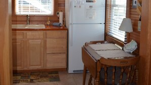 Una cocina compacta con armarios de madera, un refrigerador, un lavamanos y una mesa de comedor con una silla.