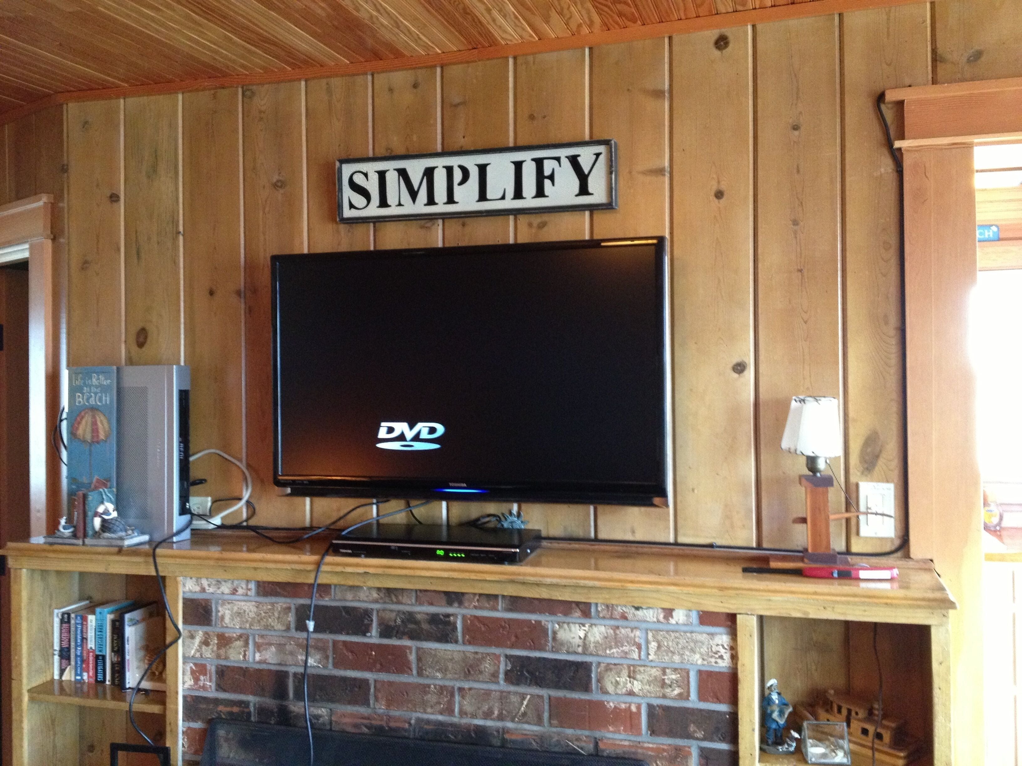 A television mounted on a wooden wall with a sign above it that reads 'SIMPLIFY'.
