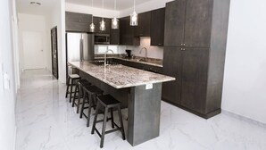 A modern kitchen with a large island, dark cabinets, and pendant lighting. - Oceanfront Villa Amor (Villas Corona)
