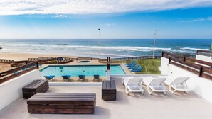 A rooftop pool with a view of the ocean, lounge chairs, and a wooden deck. - Oceanfront Villa Amor (Villas Corona)