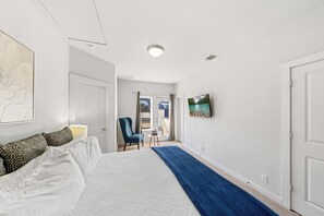 A hotel room with a large bed, a blue throw blanket, a chair, a small table, and a painting on the wall. - Fam Friendly 5 BDRM Home Blocks to Pearl, Riverwalk, and Convention Center! (San Antonio)