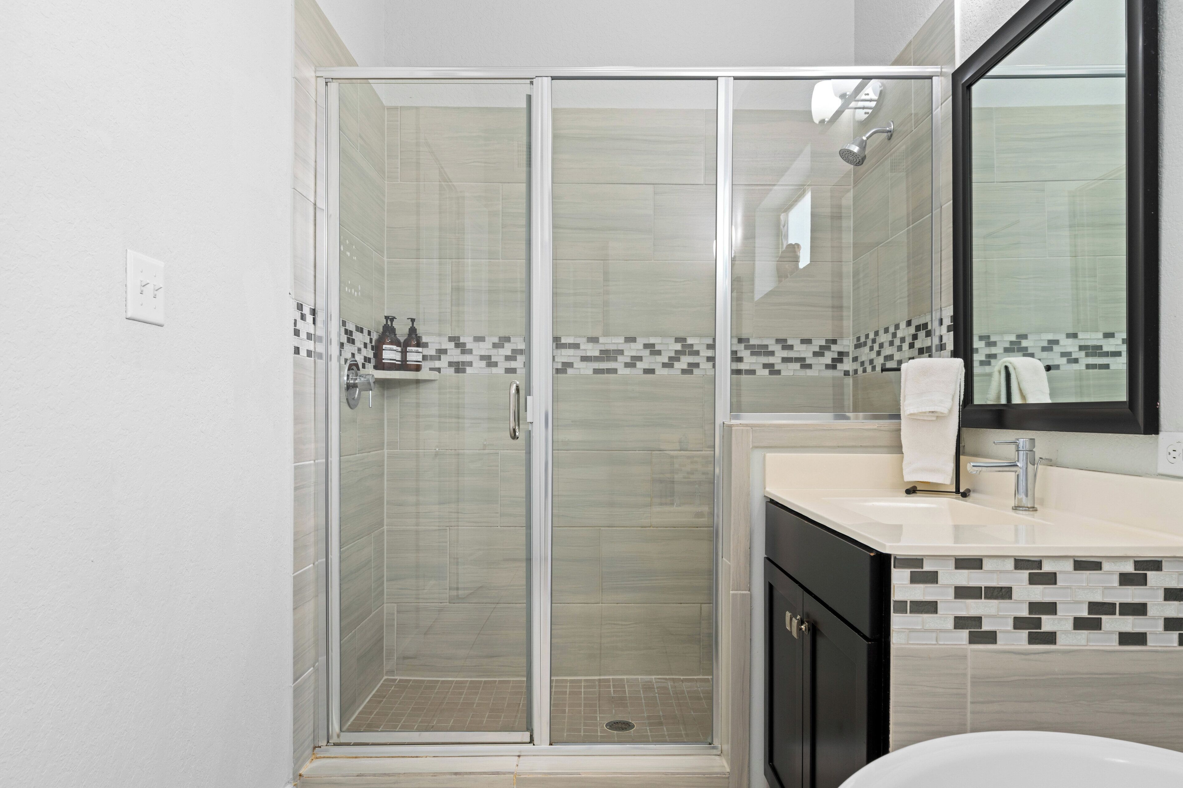 A modern bathroom with a glass-enclosed shower, a white sink, and a tiled backsplash.