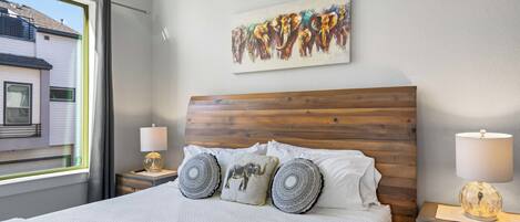 Una cama bien tendida con almohadillas estampadas, un cabecero de madera y un cuadro de un elefante colgado en la pared.
