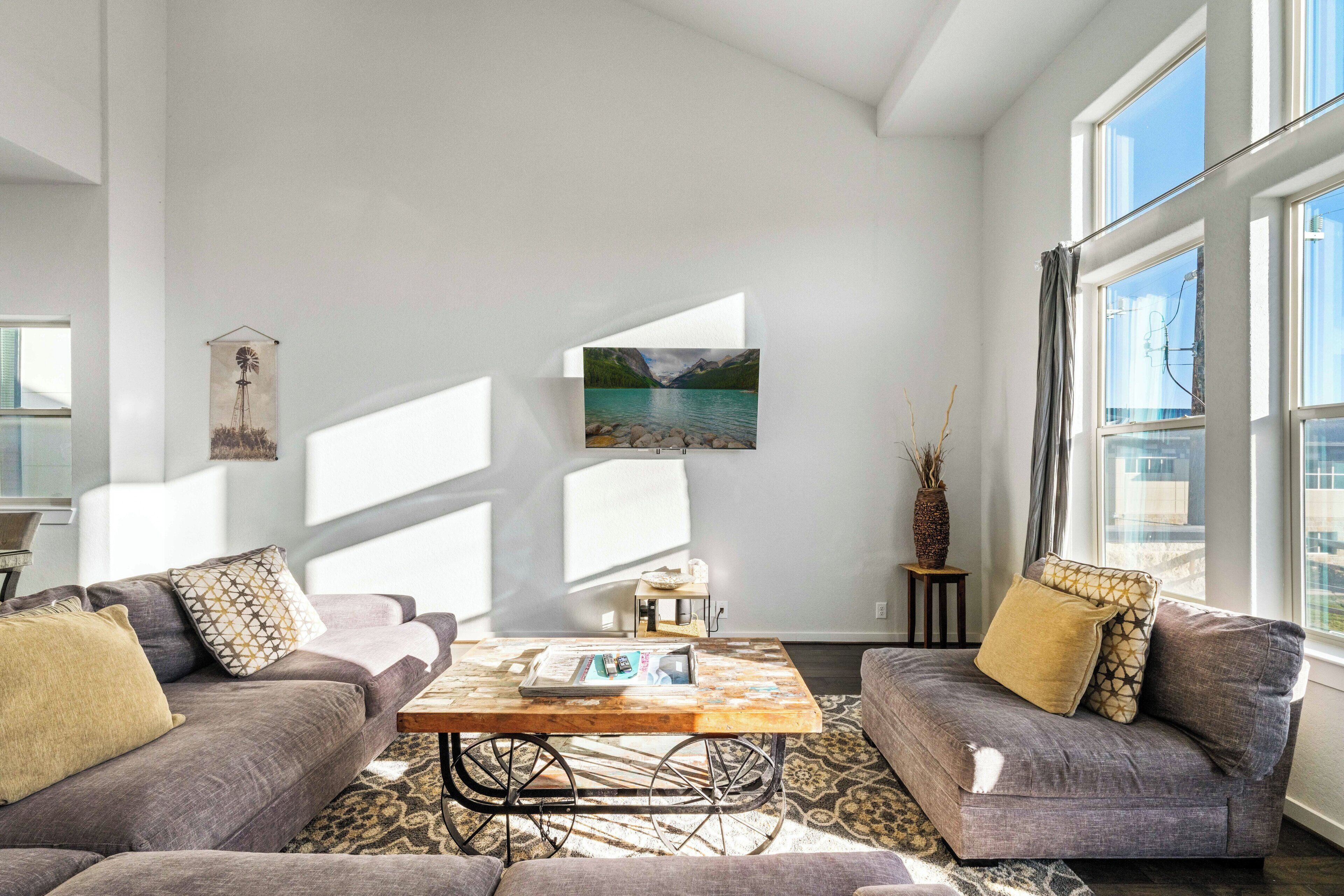 A modern living room with a grey sofa set, a coffee table, and a large window with a view of a lake.