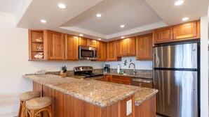 Una cocina moderna con armarios de madera, electrodomésticos de acero inoxidable, encimeras de granito y taburetes de bar.