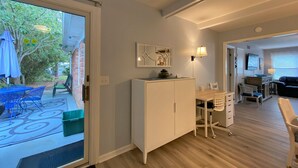 Une pièce comprenant une table à manger, des chaises, un meuble blanc, un téléviseur et une porte donnant sur un patio aménagé avec du mobilier d’extérieur.
