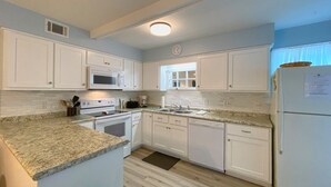 Une cuisine avec des meubles blancs, un four à micro-ondes, une cuisinière, un évier et un réfrigérateur.