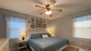 Une chambre à coucher comprenant un lit, deux tables de chevet avec des lampes, un ventilateur de plafond et des éléments de décoration murale.