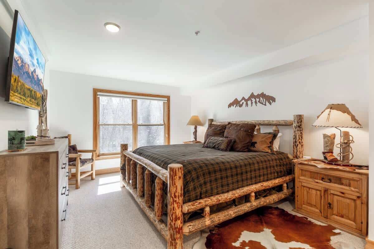A rustic bedroom with a wooden bed, a large window, and a cowhide rug.