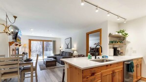 A modern kitchen with wooden cabinets, a large island with a sink, and a dining area with a table and chairs.