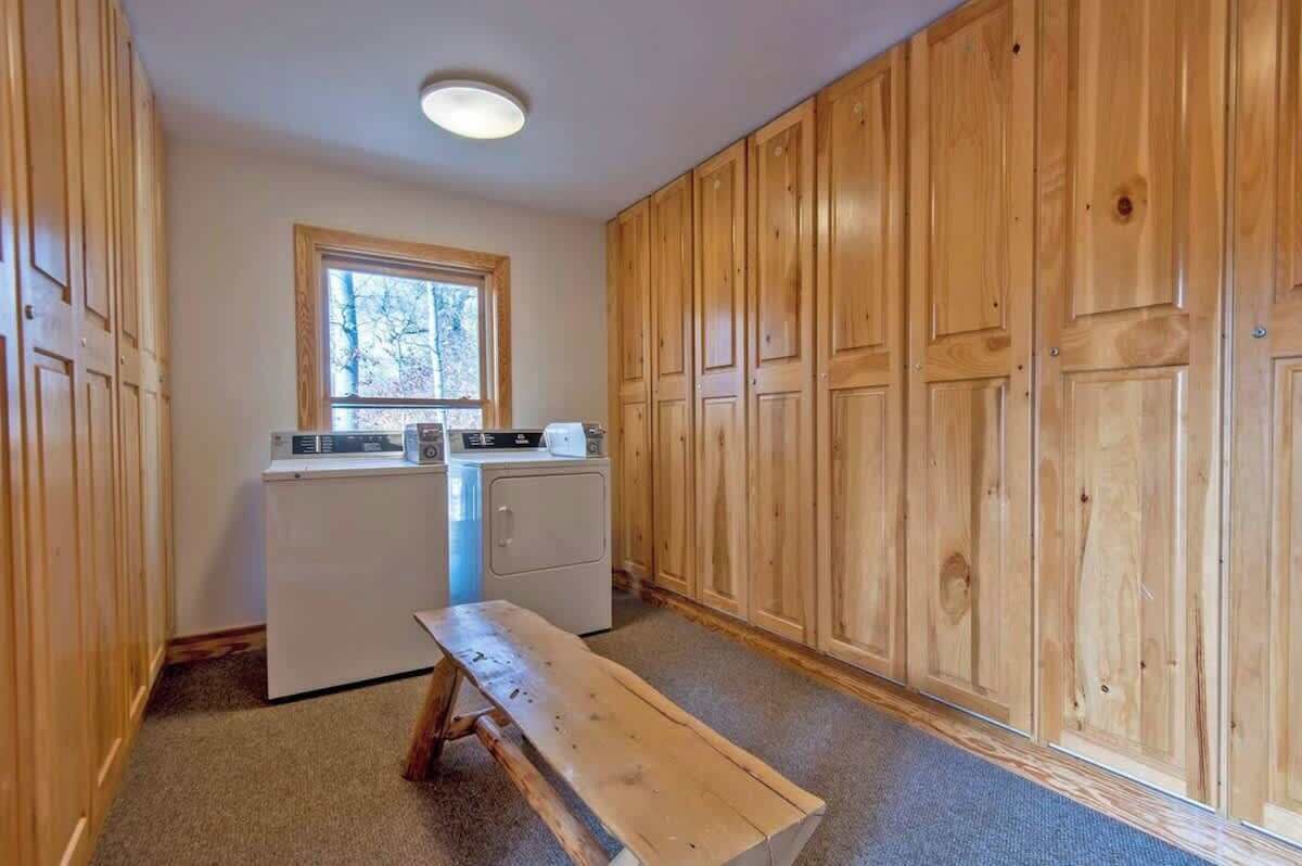 A laundry room with wooden cabinets, a washing machine, a dryer, and a bench.