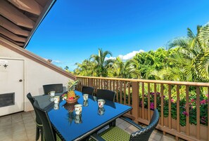 A balcony with a table set for two, surrounded by lush greenery and a clear blue sky.