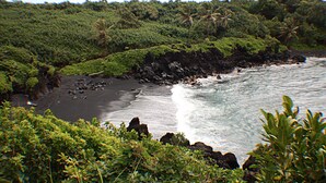 A coastal landscape with a black sand beach, rocky shoreline, and lush greenery. - Partial Ocean View from private lanai, Queen Bed.....fully furnished condo (Kihei)