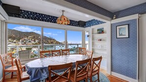 A dining area with a round table, wooden chairs, and a view of a coastal town. - 5 Bdrm Home, Vaulted Ceilings, Amazing 180 Degree Ocean View - 176 Middle Terrac (Avalon)