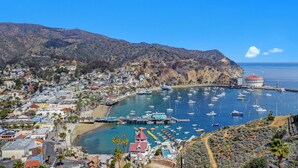 A coastal town with a marina filled with boats, a prominent building with a red roof, and a mountainous backdrop. - 5 Bdrm Home, Vaulted Ceilings, Amazing 180 Degree Ocean View - 176 Middle Terrac (Avalon)