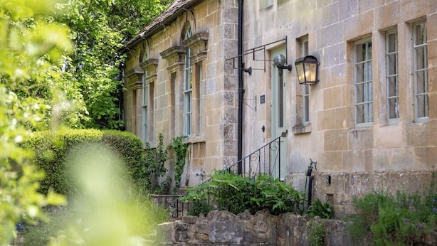 A stone building with multiple windows, a stone staircase, and a hedge in front. - The School Rooms Estate (Corsham)
