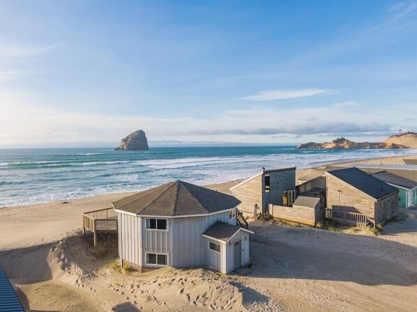 Um imóvel à beira-mar com várias cabanas de madeira, uma praia arenosa e um afloramento rochoso ao fundo.