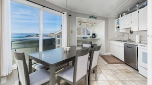 A modern kitchen with a large window overlooking the ocean, a dining area with a table and chairs, and white cabinetry.
