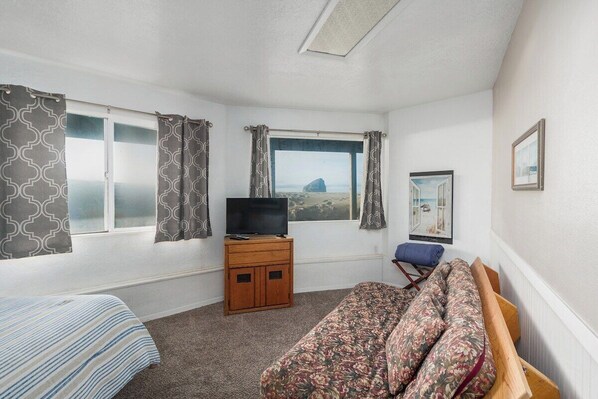 A room with a bed, a sofa, a TV on a wooden cabinet, and a window with a view of a landscape.