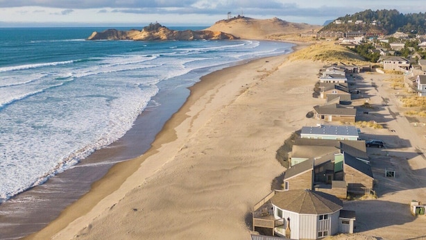 A coastal residential area with houses along the beach, a sandy shoreline, and a hilly backdrop.