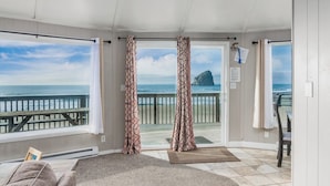 A room with a view of the ocean, a wooden deck, and a chair.