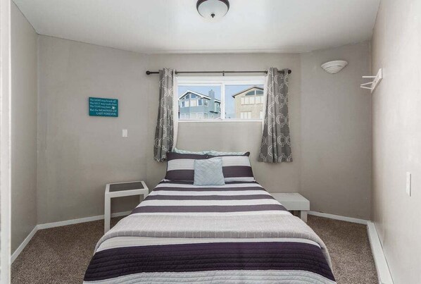 Un dormitorio con cama, ventana con cortinas, mesita de noche y estante en la pared.