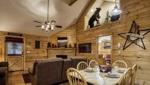 Un accogliente interno di una baita con arredamento in legno, un tavolo da pranzo per quattro persone, un divano e una ventola a soffitto.
