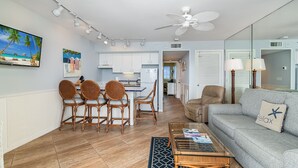 A modern living room with a grey sofa, wicker chairs, a coffee table, and a dining area with wicker chairs and a small table. - Beachfront Penthouse at the Apollo!  Best Views on Marco Island! (Marco Island)