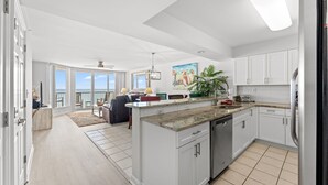 Une cuisine moderne avec des meubles blancs, un îlot central et une vue sur l’extérieur.