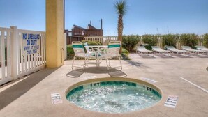 Un espace piscine avec des chaises longues, un jacuzzi et un panneau indiquant le poste de surveillance du sauveteur.