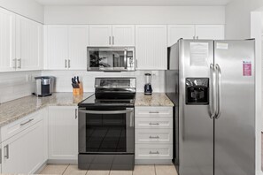 A modern kitchen with white cabinetry, a stainless steel refrigerator, a microwave, an oven, and a coffee maker.