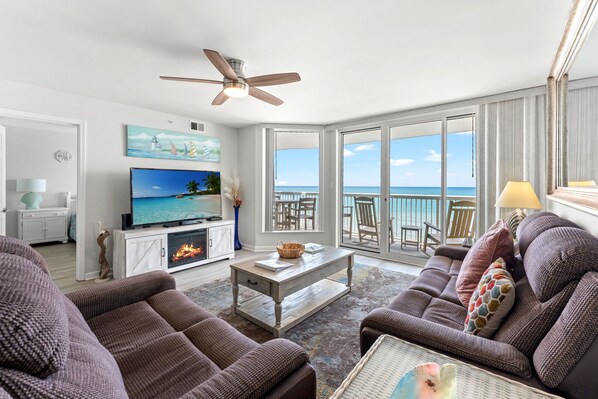 A living room with a television, fireplace, and a view of the ocean.